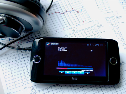 Im Bildmittelpunkt ist das Tomatis-Gerät SOLISTEN® zu sehen. Es sieht beinahe aus wie ein modernes Smartphone mit einem großen Display. Darauf kann man blaue Tastensymbole für einen CD-Player erkennen und ebenfalls in blau Balken, die wie Schwingungskurven aus der Akustik aussehen. Es ist ein Kopfhörer angeschlossen, der nur im Bildanschnitt erkennbar ist. Im Hintergrund liegen Blätter mit Diagrammen und eingezeichneten Kurven. Testergebnisse eines Hörtests.
